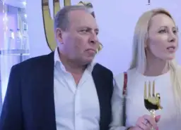 Wojtek Kurowski, wiek nieznany, w garniturze i białej koszuli, obok kobiety z złotym trofeum w kształcie dłoni.
