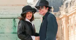 Lisa Marie Presley i jej mąż Michael Jackson w kapeluszach i okularach przeciwsłonecznych, uśmiechnięci na tle budowli.