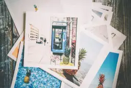 Stos odbitek ze zdjęciami: budka telefoniczna, ananasy, plaża, miasto.