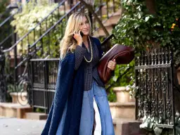 Estilo chic en la ciudad: una mujer con un abrigo azul marino y falda vaquera, combinando granate y verde con su bolso y el follaje.