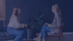 Terapeutka zajęciowa z notatnikiem rozmawia z pacjentką siedzącą na kanapie.