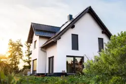 Nowoczesny biały dom z panelami słonecznymi na dachu, otoczony zielenią.