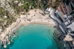 Malta: piaszczyste plaże otoczone skałami i zielenią, z turkusową wodą i kilkoma osobami odpoczywającymi na piasku.