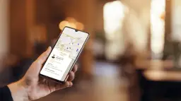 Dłoń trzyma smartfon z mapą i danymi firmy. Czy wizytówka Google jest płatna? Nie, jest darmowa, co widać na ekranie.