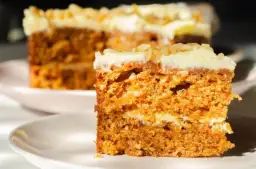 Wilgotne ciasto marchewkowe z kremowym lukrem, idealne na dietę. Pyszny kawałek na talerzyku.