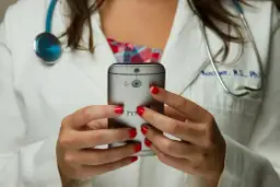 Lekarka w białym kitlu z czerwonymi paznokciami trzyma telefon. Czy pracodawca widzi kod choroby na ekranie?