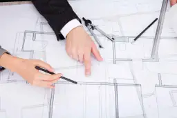 Dwie osoby analizują projekt budowlany, dyskutując, jak zaznaczyć zmiany nieistotne w projekcie.