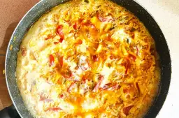 Pyszny omlet z warzywami w trakcie smażenia na patelni. Widoczne kawałki papryki i cebuli.