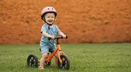 Uśmiechnięte dziecko w kasku na rowerku biegowym. Od jakiego wieku można zacząć naukę jazdy? Od ok. 18 miesiąca życia, gdy maluch pewnie stawia kroki.