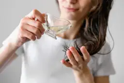 Kobieta aplikuje hydrolat na końcówki włosów. Hydrolat co to? To woda kwiatowa, która nawilża i odżywia włosy.