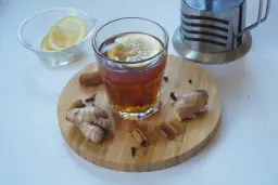 Szklanka herbaty z imbirem, cytryną i cynamonem na desce.