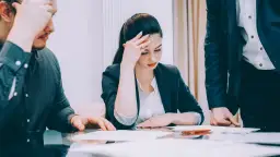 Trzy osoby przy stole analizują dokumenty. Kobieta z ręką na czole, mężczyzna drapiący się po głowie, a trzeci wskazuje na papiery. Dyskutują o sekretach ustawy o lock-upie na aktywach wnoszonych do fundacji rodzinnych.