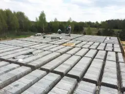 Budowa stropu teriva w toku. Betonowe pustaki ułożone w rzędach, zbrojenie gotowe do zalania. Pracownicy doglądają postępu prac.