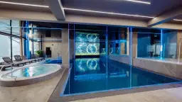 Nowoczesny basen i jacuzzi w rezydencji Aqua Szklarska Poręba. Niebieskie podświetlenie i ekran z animacją tworzą relaksującą atmosferę.