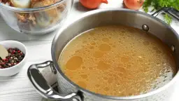 Olla con caldo de huesos burbujeante, junto a un bol con granos de pimienta y laurel, y otro con huesos.