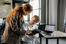 Dwóch młodych ludzi analizuje dokumenty, planując strategię multi channel marketing. Na biurku laptop, telefon i notatnik.