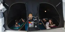 Dzieci cieszą się **campingiem dla dzieci** w namiocie. Chłopiec czyta książkę, dziewczynka bawi się z pluszakiem.