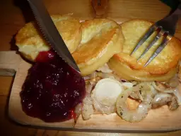 Usmażony oscypek z żurawiną, cebulą i sztućcami na desce.