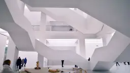 Nowoczesne muzeum sztuki z białymi, geometrycznymi schodami i kilkoma zwiedzającymi.