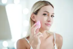 Blondynka z różową gąbeczką delikatnie muska policzek, tworząc naturalny makijaż bez podkładu.