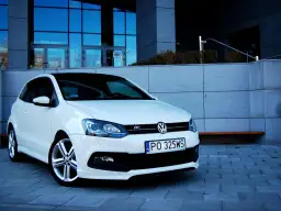 Biały VW Polo 1.2 benzyna z czarnym dachem, zaparkowany przed nowoczesnym budynkiem.