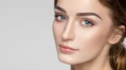 Delikatne rysy twarzy, podkreślone subtelnie zaznaczone mięśnie brody, błękitne oczy i perfekcyjny makijaż.