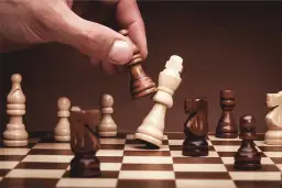 Ręka gracza wykonuje ruch, przewracając króla przeciwnika. To kluczowy moment w grze, jak się gra w szachy instrukcja.