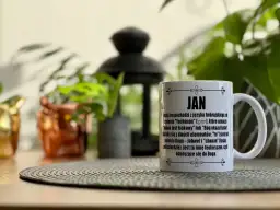 Biały kubek z napisem "JAN" i tekstem o pochodzeniu imienia, na tle roślin.