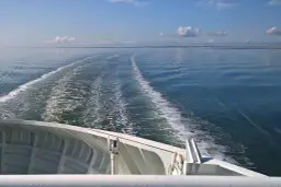 Widok z promu na fale i ślad wodny na spokojnym morzu.