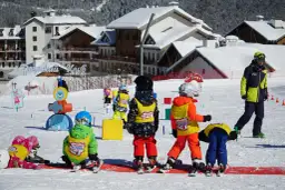 Dzieci na stoku, gotowe na ferie 2026. Wesołe kolorowe stroje narciarskie i śnieg wokół.