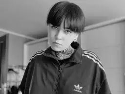 Czarno-białe zdjęcie Patrycji Widera w bluzie z kapturem Adidas. Jej twarz zdobią tatuaże i kolczyki.