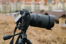 Aparat fotograficzny z obiektywem 18-300mm na statywie, z rozmytym budynkiem w tle.