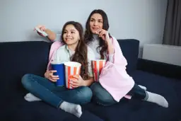 Mama i córka oglądają filmy dla nastolatków, zajadając popcorn i popijając napoje.