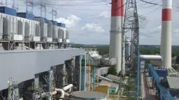 Duże budynki elektrowni z niebieskimi elementami, wysokie kominy z czerwonymi pasami i linie energetyczne.