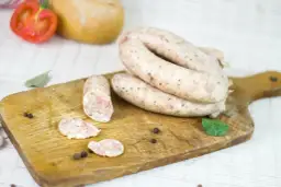 Biała kiełbasa na desce, obok pomidor, czosnek i przyprawy. Zastanawiasz się, ile czasu moczymy jelita do kiełbasy?