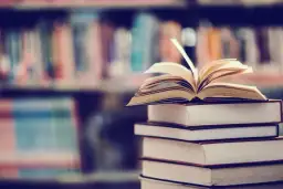 Stos książek, na wierzchu otwarta księga. W tle regały pełne literatury, w tym podręczniki do prawa pracy.