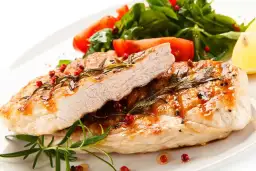 Jugoso solomillo de pavo a la parrilla, adornado con romero y pimienta rosa, acompañado de ensalada fresca y limón.