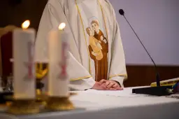 Szczegół szaty kapłańskiej z haftem świętego z dzieckiem, świece i mikrofon.