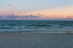 Plaża nad Bałtykiem o zachodzie słońca z różowymi chmurami i spokojnym morzem.
