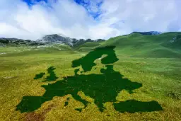 Mapa Europy w kształcie zielonej trawy na tle gór i błękitnego nieba.