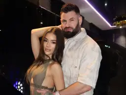 Wojtek Gola z dziewczyną, w eleganckich strojach, pozują do zdjęcia w nastrojowym oświetleniu.