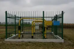 Ogrodzony obiekt gazowy z żółtymi rurami. Widać znaki ostrzegawcze. Obraz pokazuje odległość budynku od gazociągu wysokiego ciśnienia.