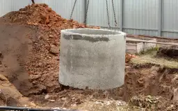 Betonowy krąg opuszczany do wykopu. Zastanawiasz się, ile kosztuje założenie szamba? To pierwszy krok do jego budowy.