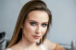 Kobieta z brązowymi włosami i niebieskimi oczami, idealnie dobrany kolor włosów do niebieskich oczu. Długie, błyszczące kolczyki.