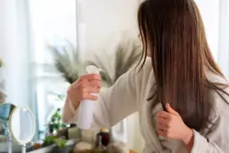 Kobieta w szlafroku spryskuje włosy odżywką w sprayu.