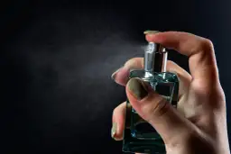 Dłoń trzymająca buteleczkę perfum i rozpylająca mgiełkę.