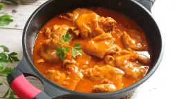 Manitas de cerdo en salsa roja, un plato tradicional español, servido en una sartén negra con perejil fresco.