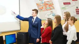 Młody technik ekonomista tłumaczy wykres na tablicy interaktywnej grupie uczniów.