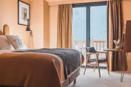 Chambre d'hôtel avec lit douillet, vue sur les montagnes enneigées et télécabines.
