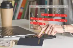 Planowanie urlopu zgodnie z kodeksem pracy. Na biurku laptop, paszport, pieniądze i kalendarz z zaznaczonymi dniami.